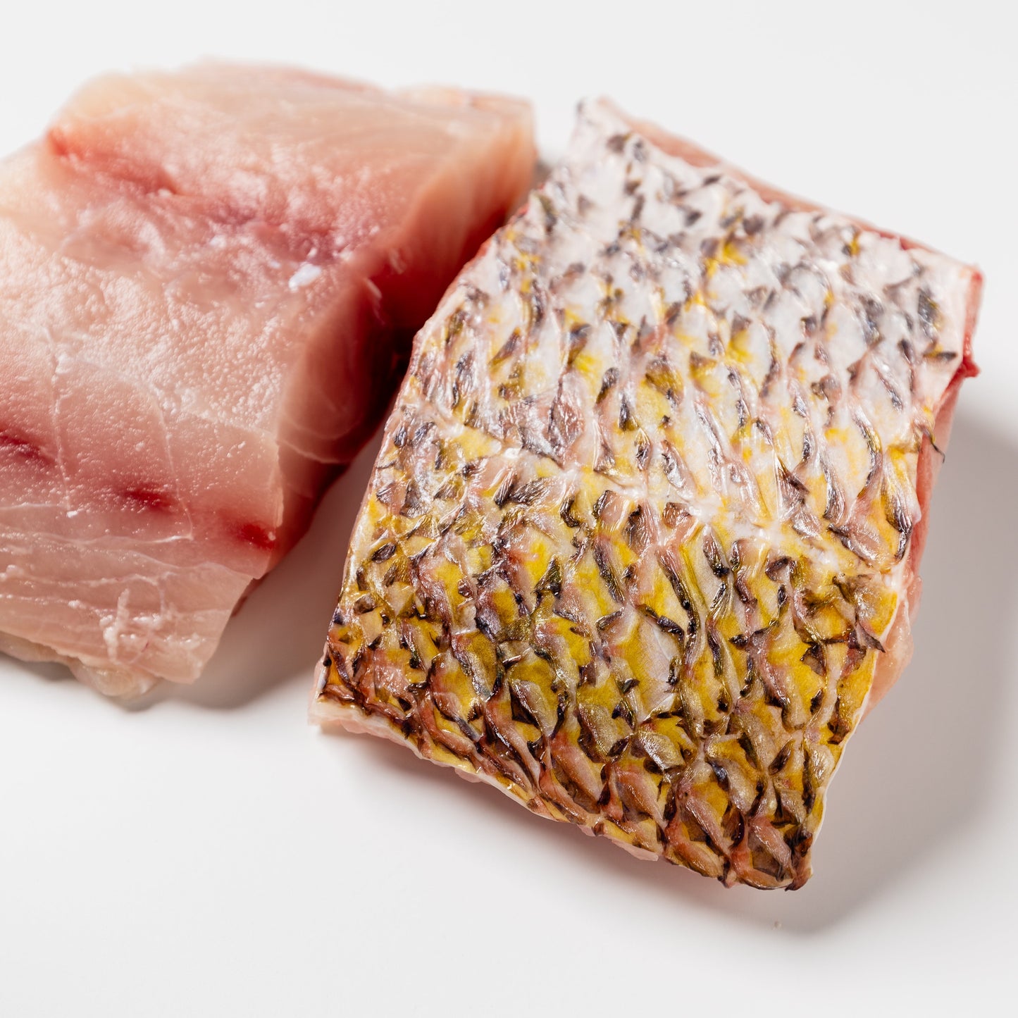 
                  
                    Two pieces of raw fish, one pink and one with a patterned skin, on a white background.
                  
                